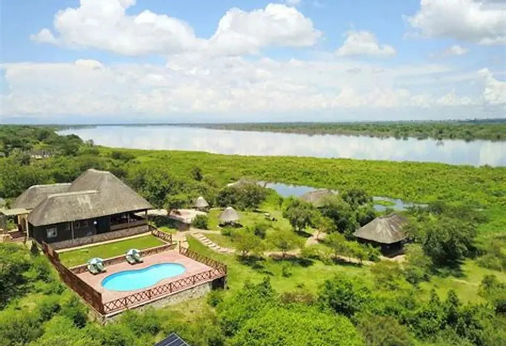 Aerial view of Buffalo Safari Lodge showing a thatched main building, swimming pool and cottages beside a river and wetlands
