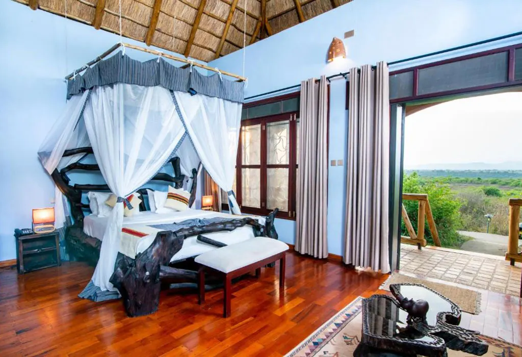 Double cottage room at Buffalo Safari Lodge with a canopy bed, polished wooden floor and open doors to savanna views-3-Day Queen Elizabeth Park Safari