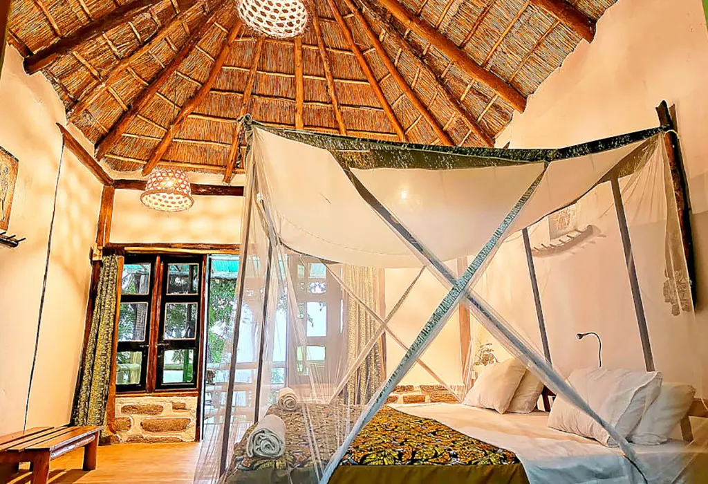 Double room at Pumba Safari Cottages with a mosquito net over the bed, wooden windows and a high thatched ceiling. 3-Day Queen Elizabeth Park Safari