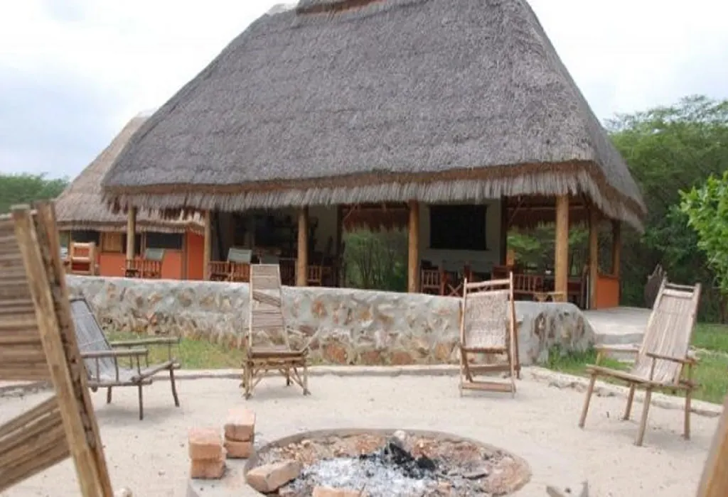 Thatched dining and lounge building at Pumba Safari Cottages with stone wall, wooden chairs and a campfire pit in front.