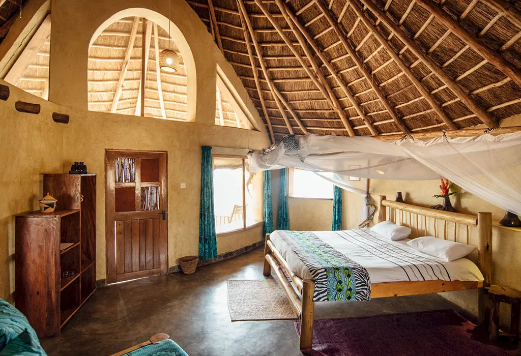 Rustic bedroom with a log-framed double bed, white mosquito net, mud-plastered walls and a high thatched ceiling